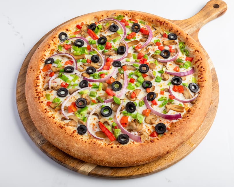 A whole vegetarian pizza with mushrooms, olives, red onions, and bell peppers on a wooden board.
