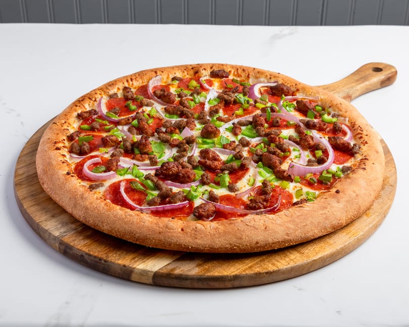A whole pepperoni, sausage, green pepper, and red onion pizza on a wooden serving board.