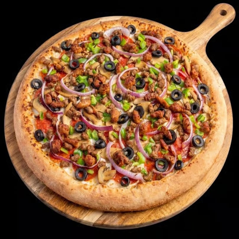 A whole pizza with sausage, mushrooms, green peppers, red onions, and black olives on a wooden peel.
