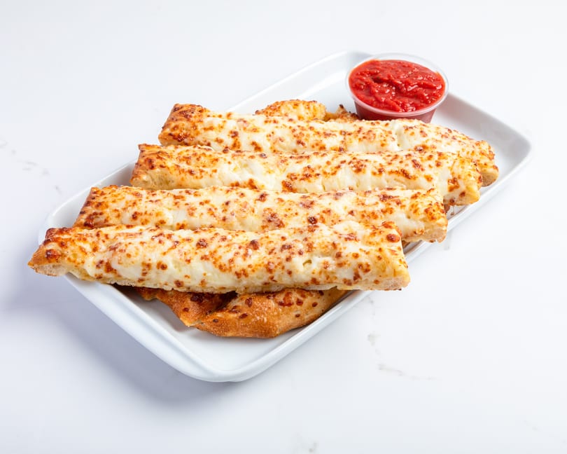 Cheesy breadsticks with a side of marinara sauce on a white rectangular plate.
