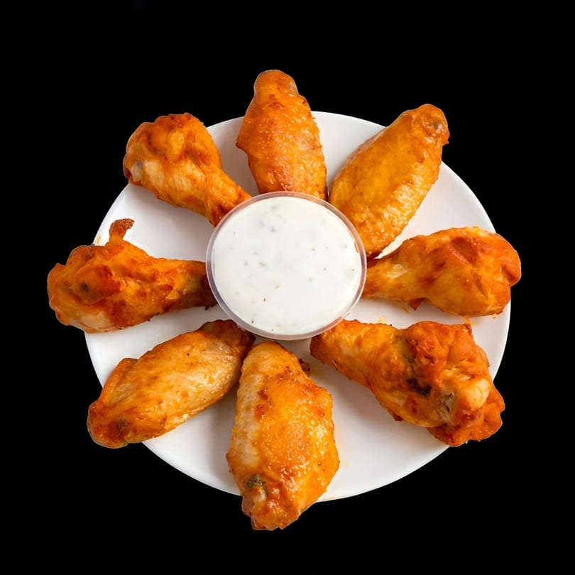 A white plate with eight buffalo chicken wings arranged around a cup of ranch dressing.