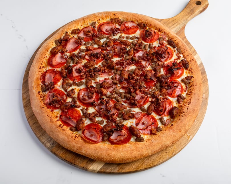 A whole meat lover's pizza with pepperoni, sausage, and bacon on a wooden paddle.