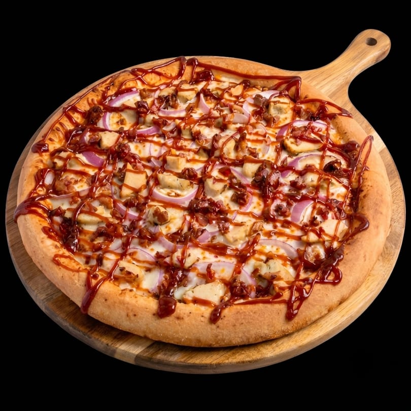 BBQ chicken pizza with red onions and bacon on a wooden serving board.