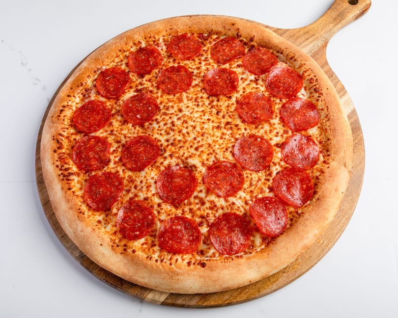 A whole pepperoni pizza with a golden crust on a wooden serving board.