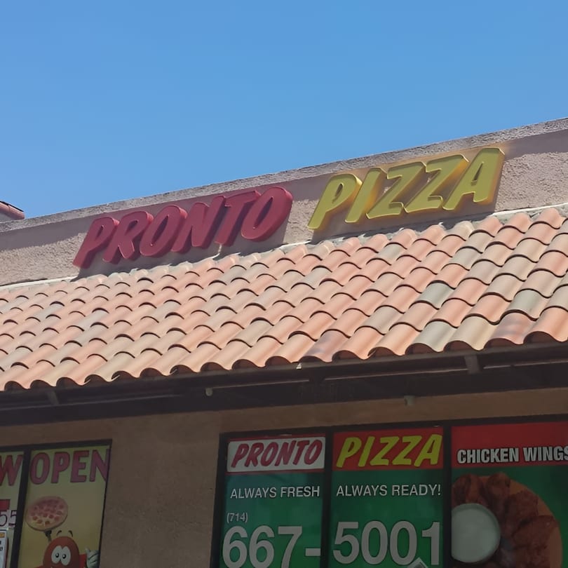 Pronto Pizza sign with red and yellow letters above a terracotta tiled roof and storefront signs.